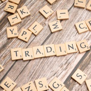 Wooden Scrabble tiles spelling 'TRADING' against a rustic wood background.